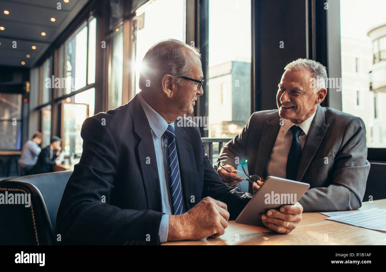 Zwei leitende Geschäftsleute haben ein informelles Treffen im Café. Geschäftsmann hält ein digitales Tablet und spricht mit seinem männlichen Partner, während er im modernen Co sitzt Stockfoto