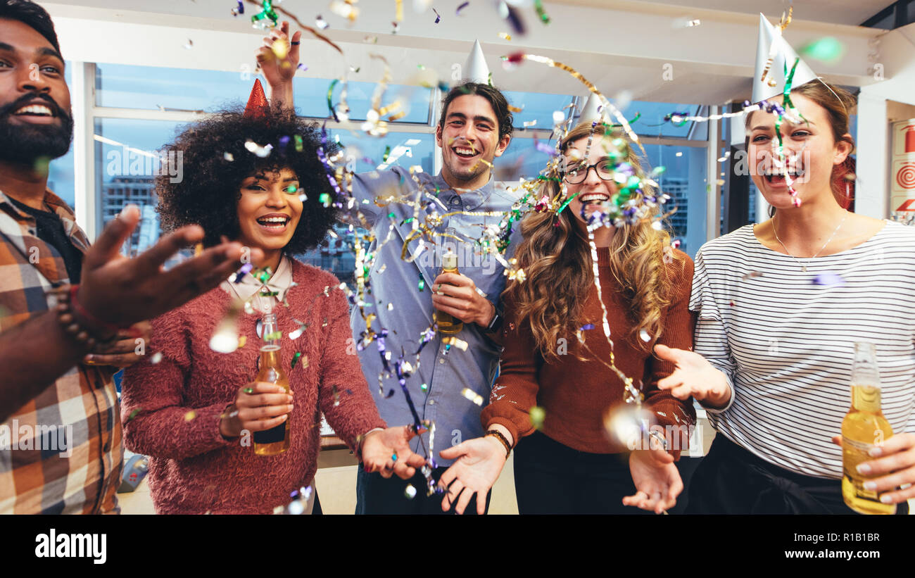Happy Geschäftsmänner und Frauen halten Getränke Spaß auf einer Party. Freunde mit einem get together party Drinks genießen mit Konfetti fliegen herum. Stockfoto