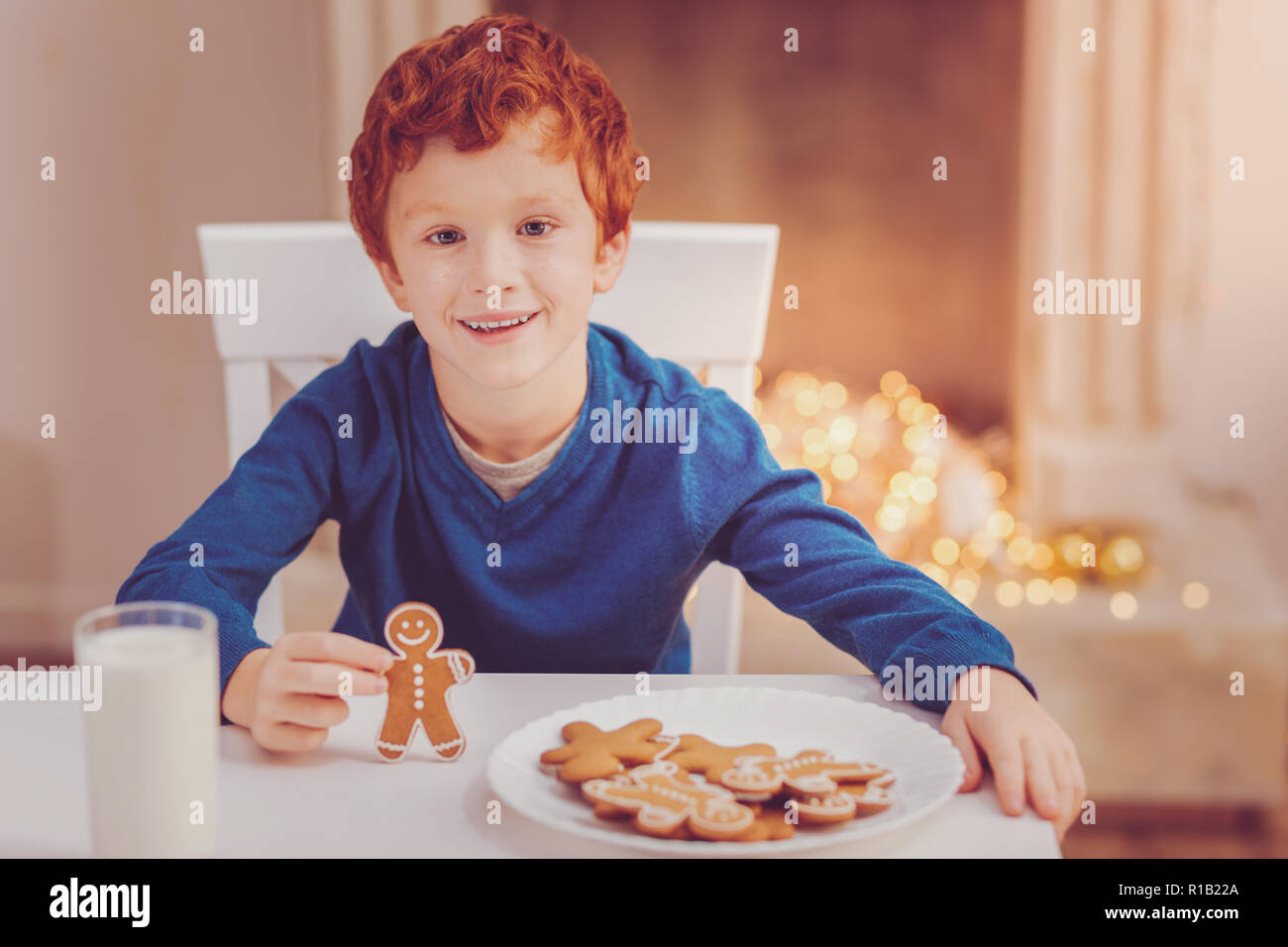 Angenehme Junge an den Tisch stellen und halten Gingerbread Man Stockfoto