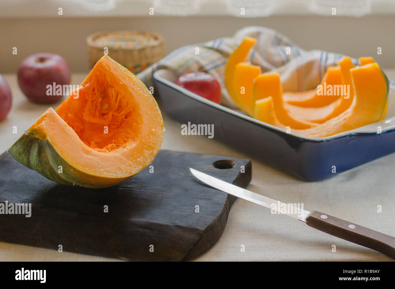 Eine orange-grün Kürbis liegt auf einem braunen Holz Schneidebrett und in einem blauen Keramik Auflaufform Stockfoto