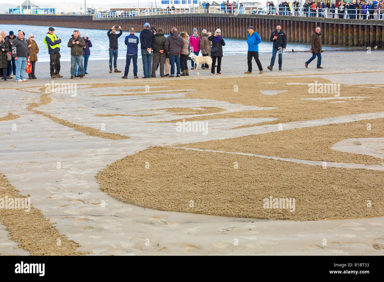 Dorchester, Dorset UK. 11. Nov 2018. Gemeinschaften in Großbritannien sammeln auf Stränden zu 100 Jahre seit dem Waffenstillstand und dem Ende des Ersten Weltkriegs markieren; zu sagen Danke und auf Wiedersehen, die Millionen von Männern und Frauen, die ihre Ufer während des Krieges verlassen, viele nie zurück. Danny Boyle's einzigartigen Seiten des Meeres, wo ein Porträt eines Einzelnen aus dem Ersten WK1 aus dem Sand entsteht und dann, als die Flut steigt, es ist weggespült. Credit: Carolyn Jenkins/Alamy leben Nachrichten Stockfoto