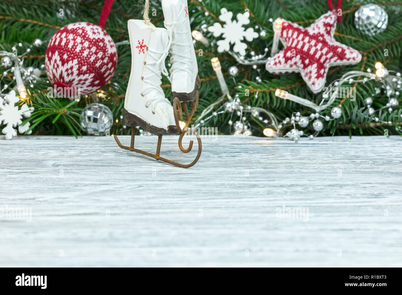 Kleine hölzerne Schlittschuhe gegen Fir Tree Branch Hintergrund mit weihnachtlichen Ornamenten verziert verschwommen Stockfoto
