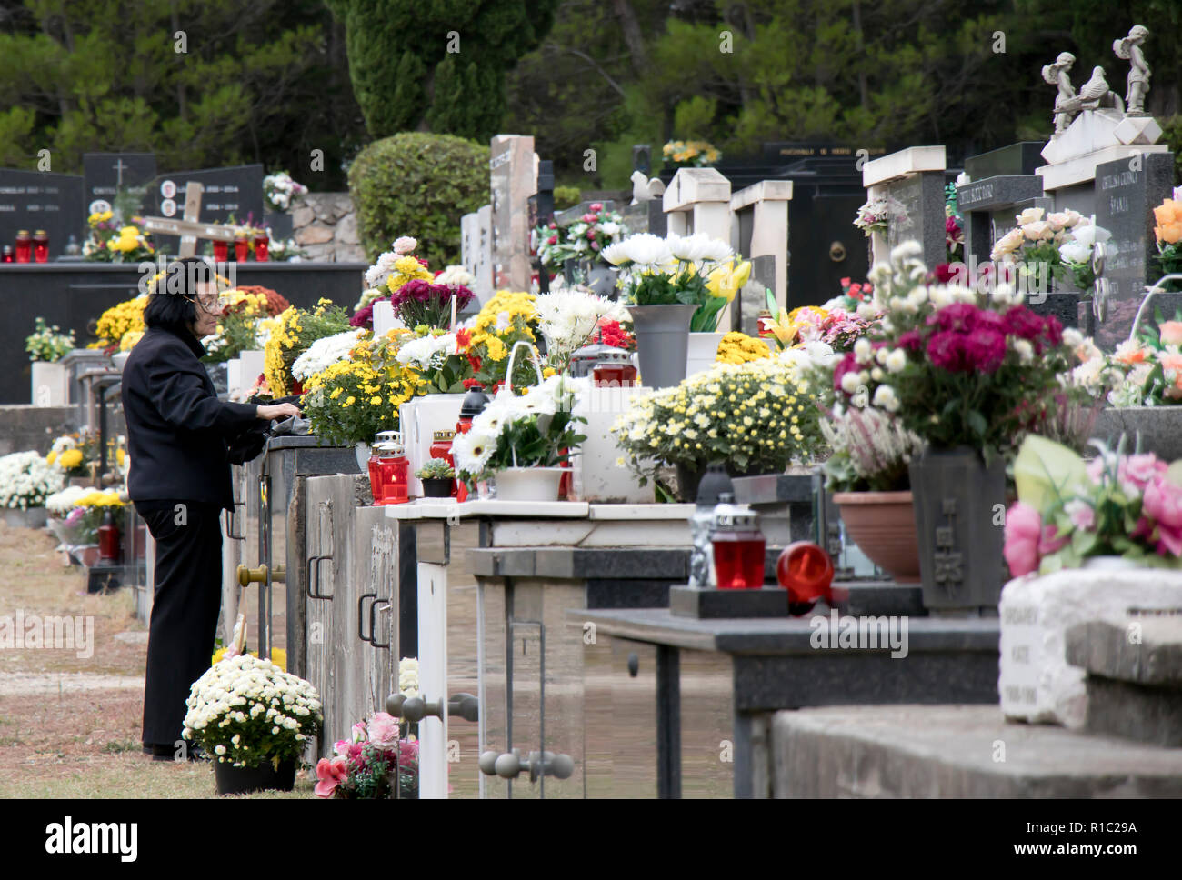 Vodice, Kroatien - November 1, 2018: Frau mit schwarzen stehend auf dem Friedhof voller Blumen und Kerzen auf den Gräbern, auf Allerheiligen Stockfoto