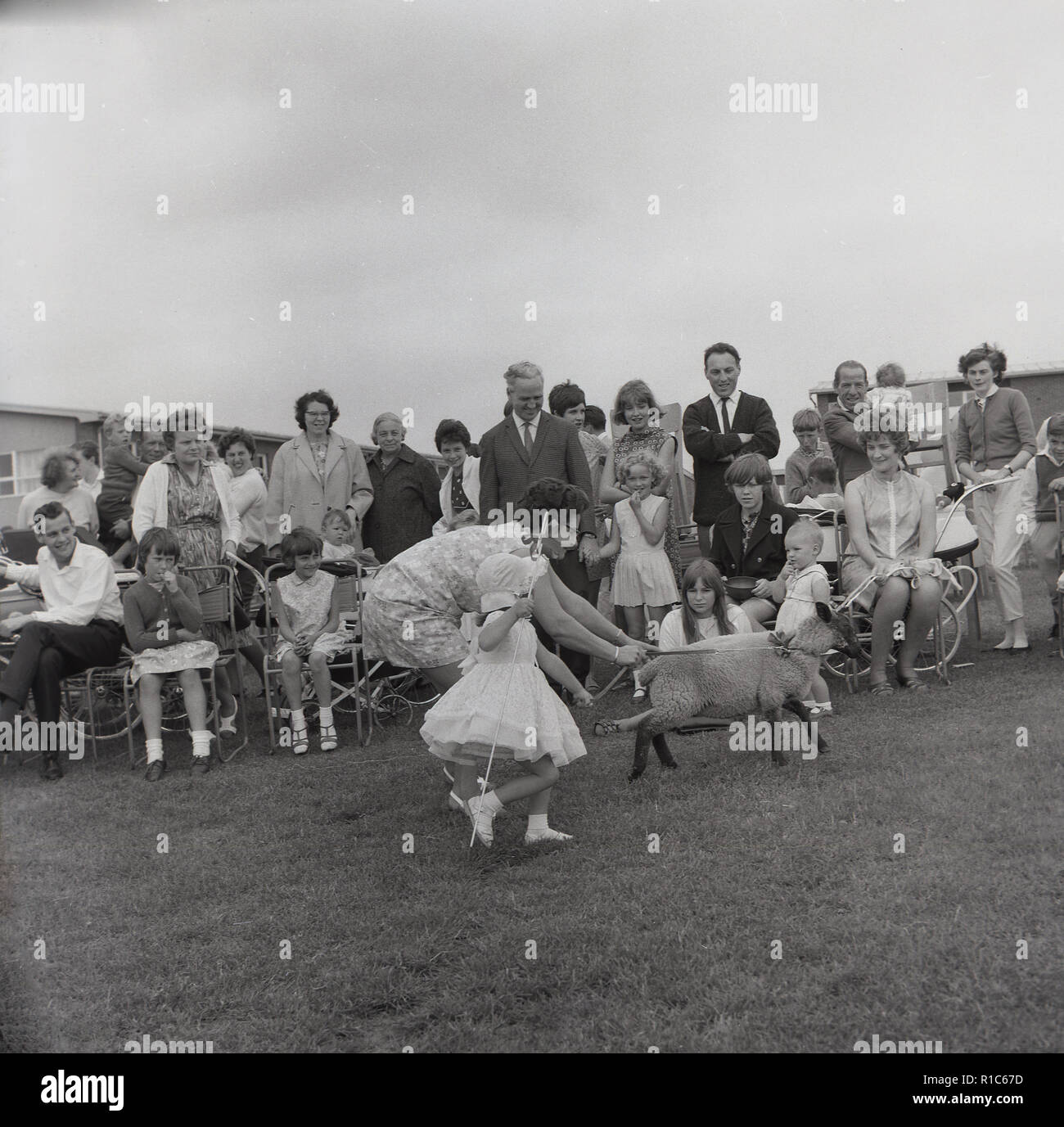 1967, historische, in einem englischen Dorf Sommer Fete, eine Mutter und ihre Tochter als "gekleidet wenig Bo-peep", eine Figur aus der beliebten Kinder Kinderlieder über eine Schäferin, laufen in einem Feld mit kleinen Schaf oder Lamm, England, UK. Stockfoto