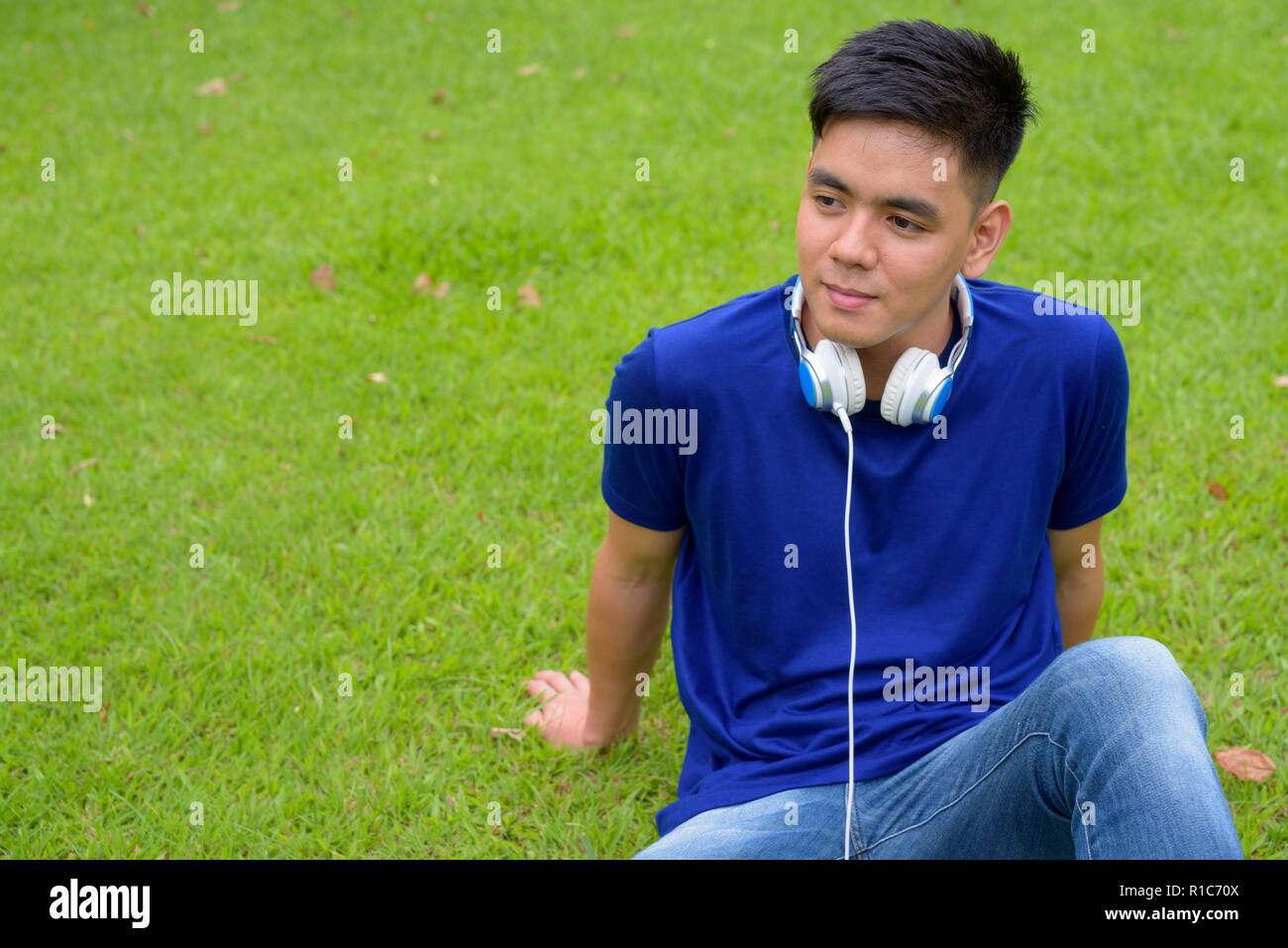 Die Jungen gut aussehenden asiatischer Mann Entspannung im Park mit Kopfhörern Stockfoto