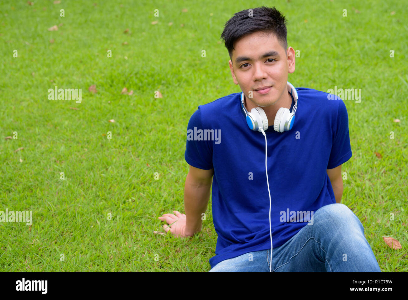 Die Jungen gut aussehenden asiatischer Mann Entspannung im Park mit Kopfhörern Stockfoto