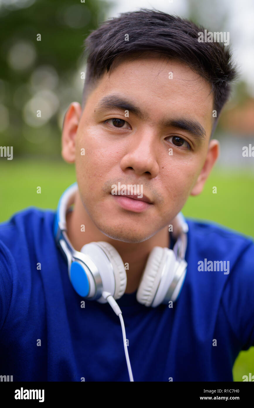 Die Jungen gut aussehenden asiatischer Mann Entspannung im Park das Tragen von Kopfhörern Stockfoto