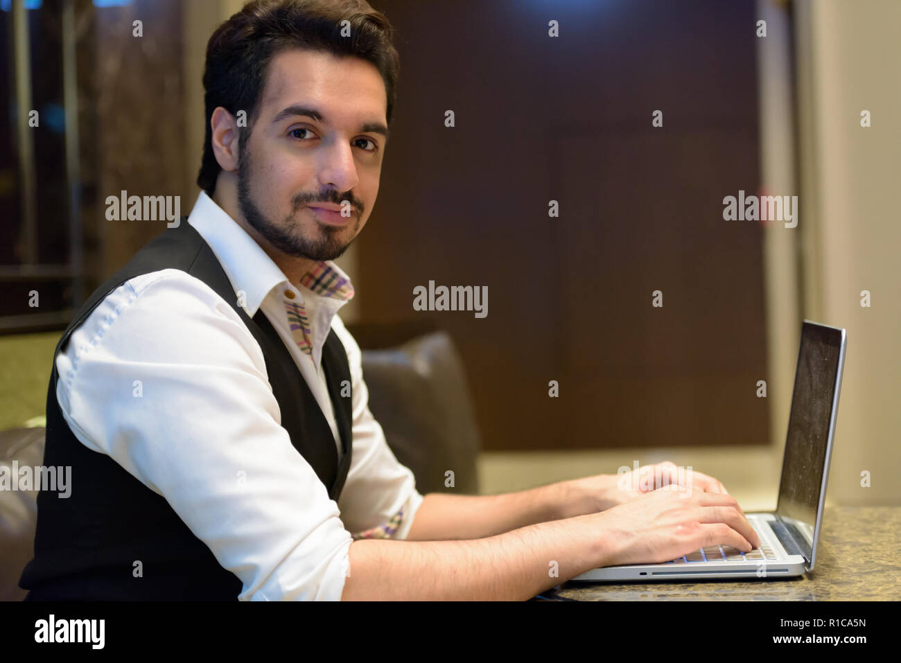 Junge schöne Indische Mann mit Laptop in der Lobby des Hotel Stockfoto