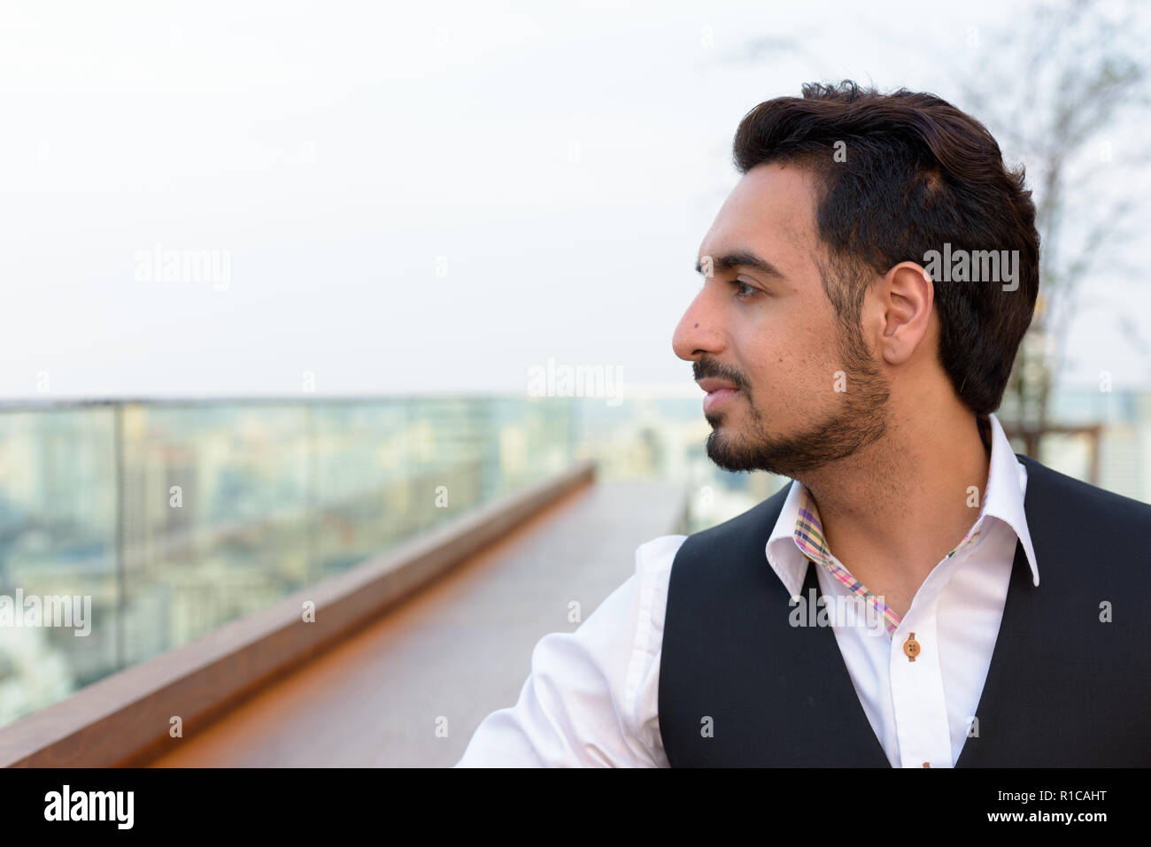 Profil anzeigen von jungen schönen Indischen Mann denken, der auf dem Dach re Stockfoto