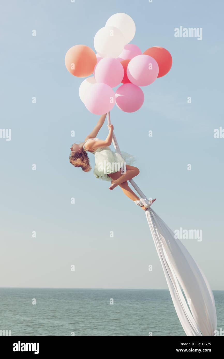 Mädchen schwebt in der Luft von Luftballons. Sie klammert sich an die Leinwände. Stockfoto