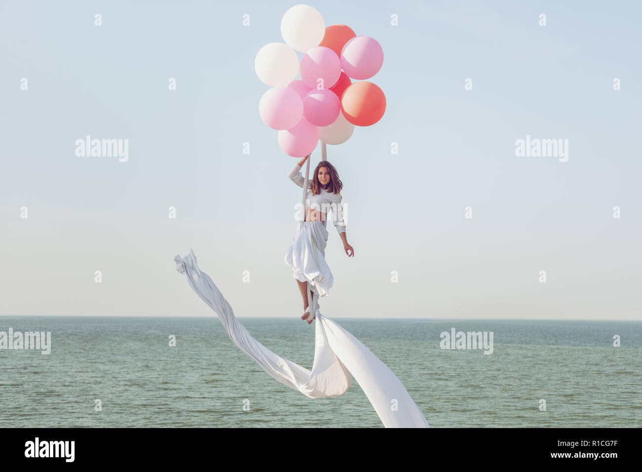 Junge Frau in einem weißen Anzug schwebt in der Luft in Luftballons. Stockfoto