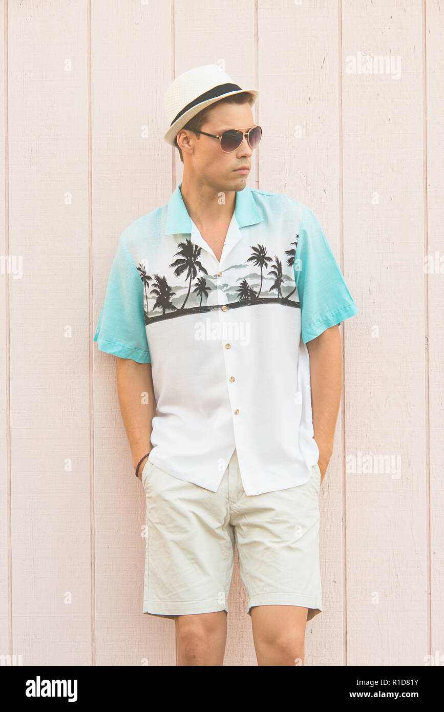 Ein schönes männliches Modell im Sommer Kleidung outdoor gegen eine einfache hölzerne Wand posieren. Er trägt einen weißen fedora Hut und Pilotenbrillen. Stockfoto