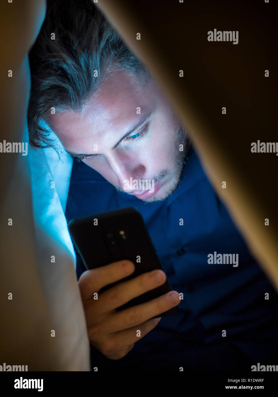 Die jungen Menschen selbst versteckt sich unter einer Decke, während Sie ein Handy zum Surfen im Internet oder für online privat chatten Stockfoto