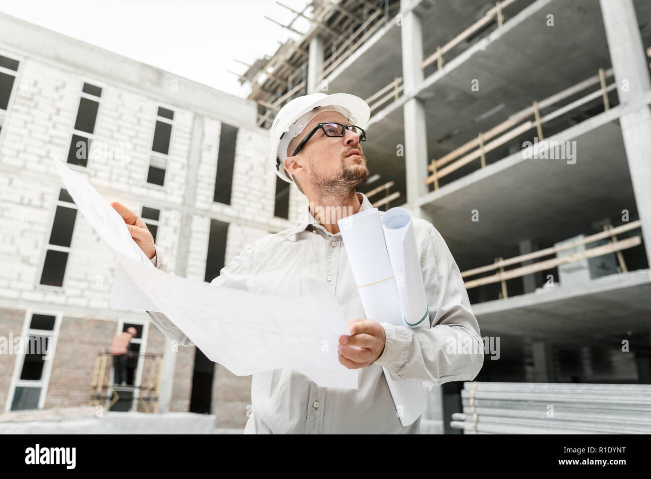 Bauingenieur in einem weißen hardhat Inspektion Blueprints auf einer Baustelle. Entwicklung und Konstruktion Industrie Konzept Stockfoto