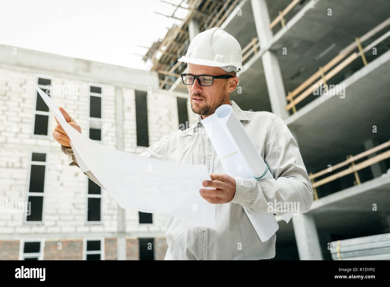 Bauingenieur in einem weißen hardhat Inspektion Blueprints auf einer Baustelle. Entwicklung und Konstruktion Industrie Konzept Stockfoto