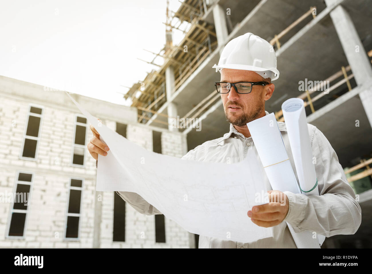 Bauingenieur in einem weißen hardhat Inspektion Blueprints auf einer Baustelle. Entwicklung und Konstruktion Industrie Konzept Stockfoto