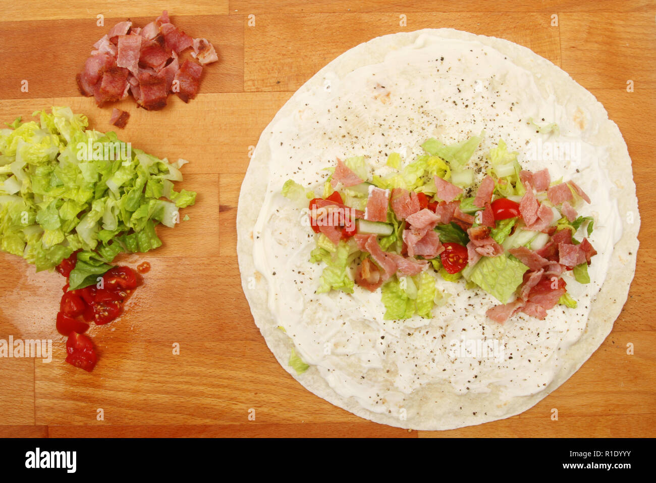 Zutaten für eine Speck Salat und Tomate Sandwich wrap auf einer hölzernen Schneidebrett, Ansicht von oben Stockfoto