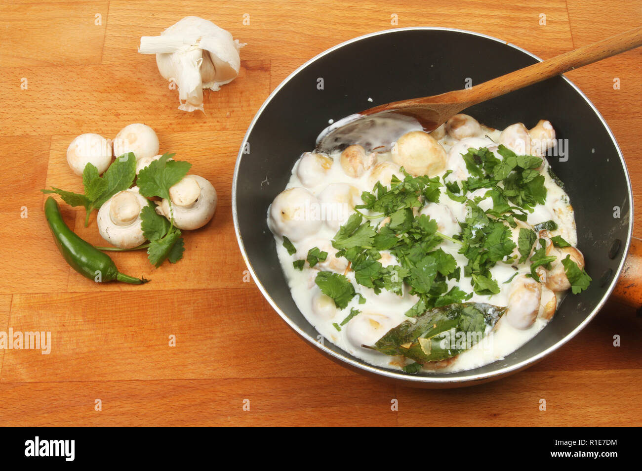 Baby Champignons in einer Creme und Kräutersoße im Wok mit Zutaten auf einem hölzernen Arbeitsplatte Stockfoto