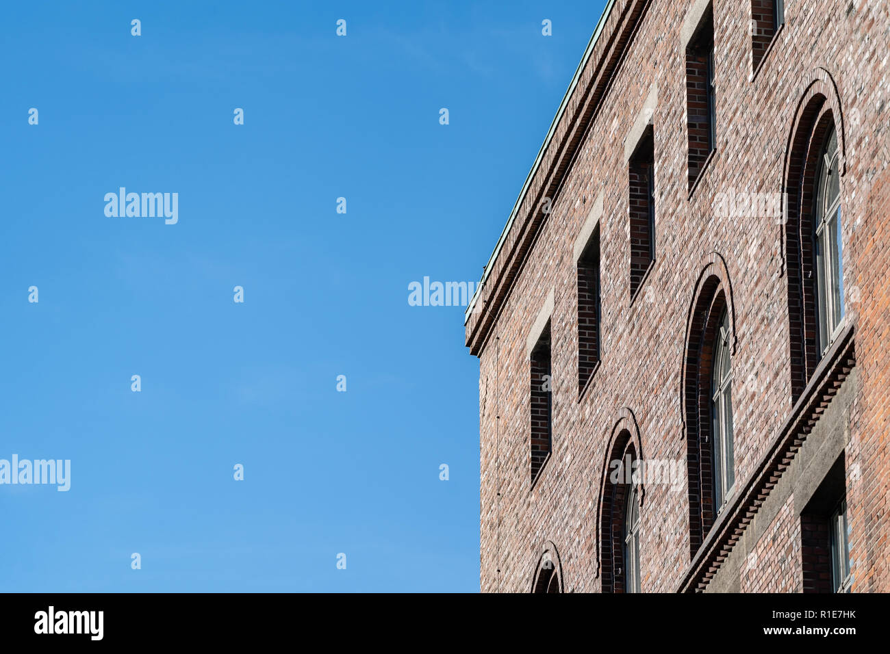 Obere Ecke von Backstein Fassade mit Bogenfenstern, von niedrigen Winkel gegen den klaren blauen Himmel gesehen. Stockfoto