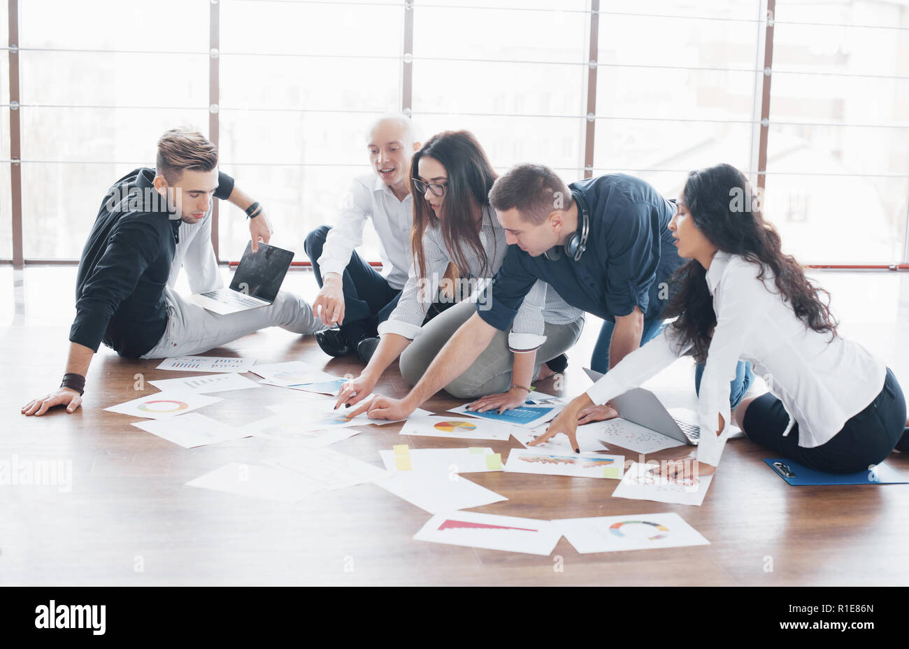 Junge kreative Menschen in modernen Büro. Die Gruppe junger Geschäftsleute gemeinsam mit Laptop. Freiberufler sitzen auf dem Boden. Zusammenarbeit corporate Achievement. Teamwork Konzept Stockfoto