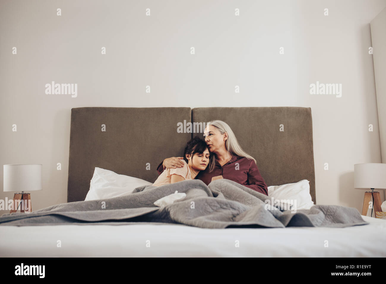 Ältere Frau, die ihre Tochter in den Arm und Küssen mit dem Kopf. Mutter und Tochter auf dem Bett sitzen zusammen. Stockfoto