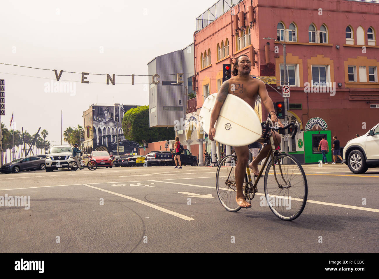 Ein Surfer zu Hause auf seinem Fahrrad mit Surfbrett am Venice Beach, Los Angeles, Kalifornien Stockfoto