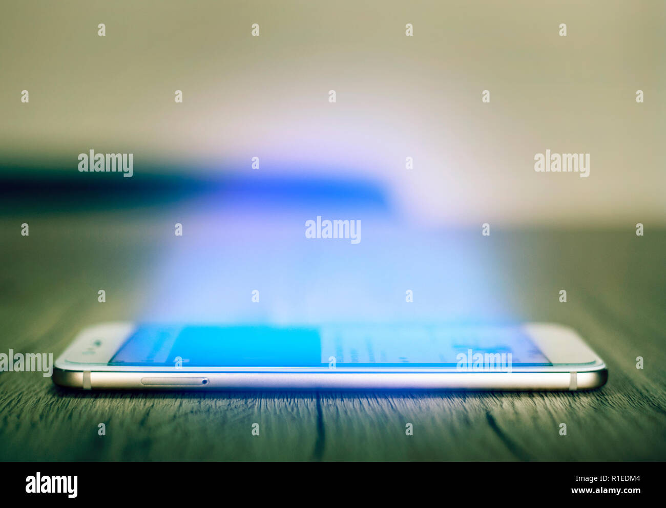Seitenansicht des Smartphone auf dem Holztisch mit einladenden blauen Licht leuchten aus dem Bildschirm. Süchtig Konzept zu Internet. Selektiver Fokus auf Stockfoto
