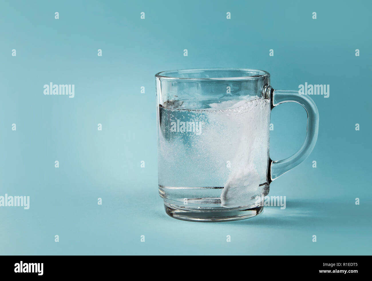 Seitenansicht des löslichen Schmerzmittel Auflösen in Wasser sprudelt, ganz klares Glas Schale, auf blauem Hintergrund. Stockfoto
