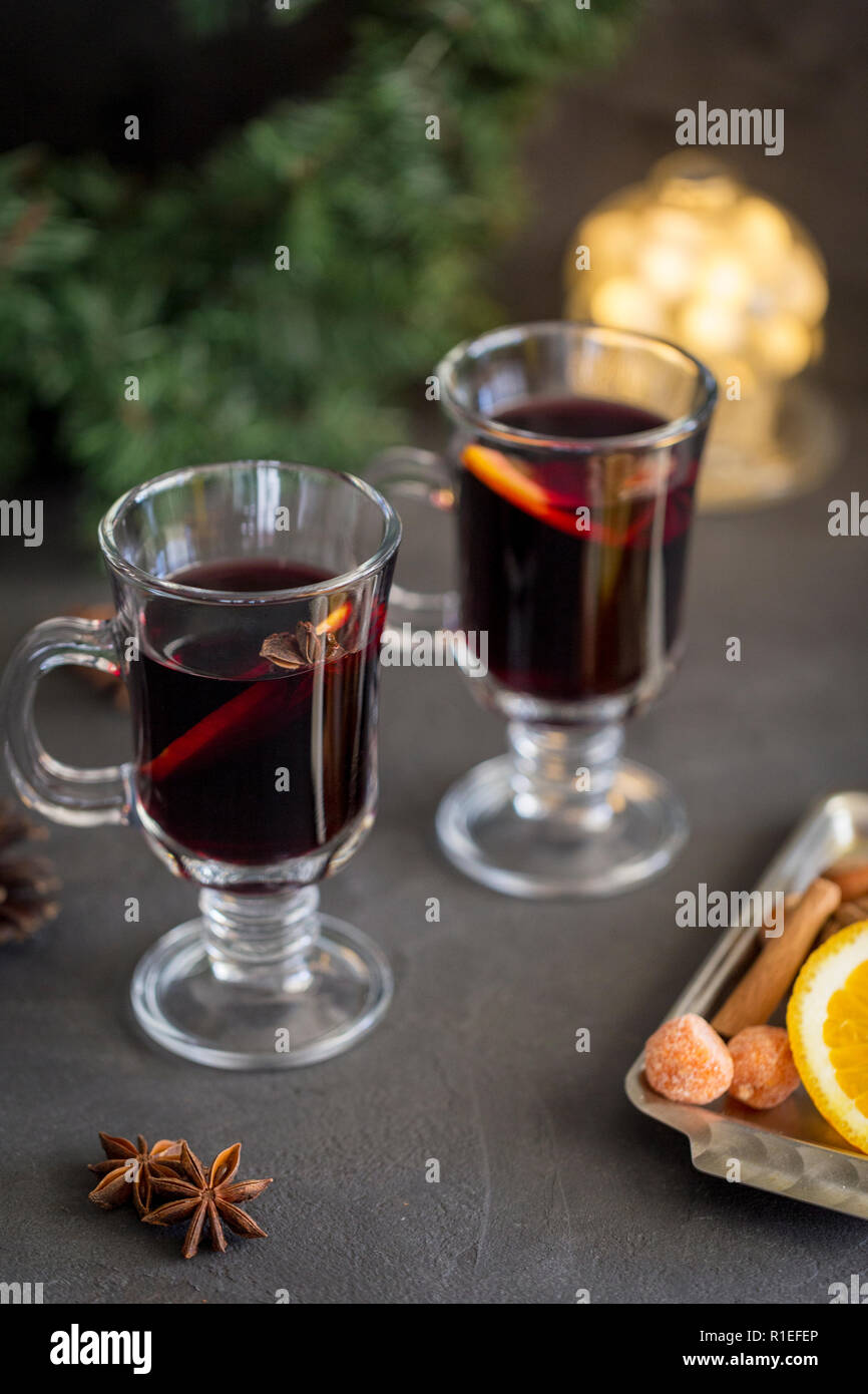 Winter Zusammensetzung. Glühwein in Gläsern auf schwarzen Hintergrund. Tanne Kranz, Lichter, Fach mit Orange, Zimt, Nüssen und Gewürzen in der Nähe. Stockfoto
