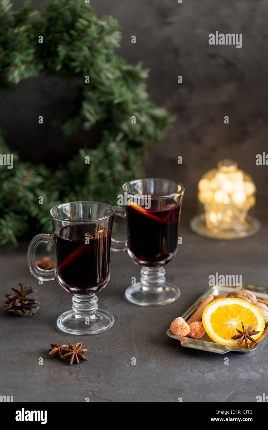 Winter Zusammensetzung. Glühwein in Gläsern auf schwarzen Hintergrund. Tanne Kranz, Lichter, Fach mit Orange, Zimt, Nüssen, Kegel und Gewürze in der Nähe. Stockfoto