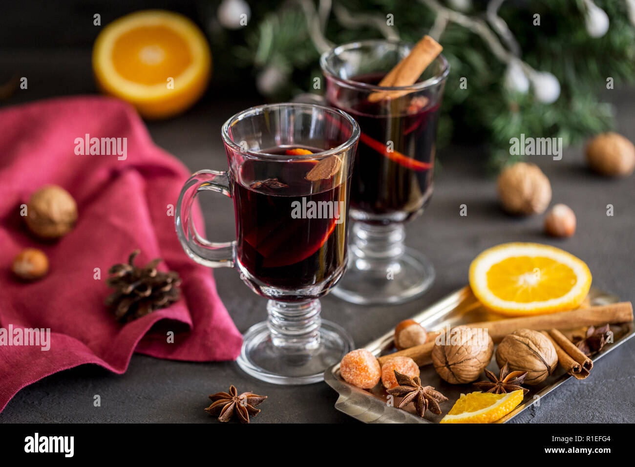 Winter Zusammensetzung. Glühwein in Gläsern auf schwarzen Hintergrund. Tanne Kranz, Fach mit Orange, Zimt, Nüssen, Kegel und Gewürze in der Nähe. Stockfoto