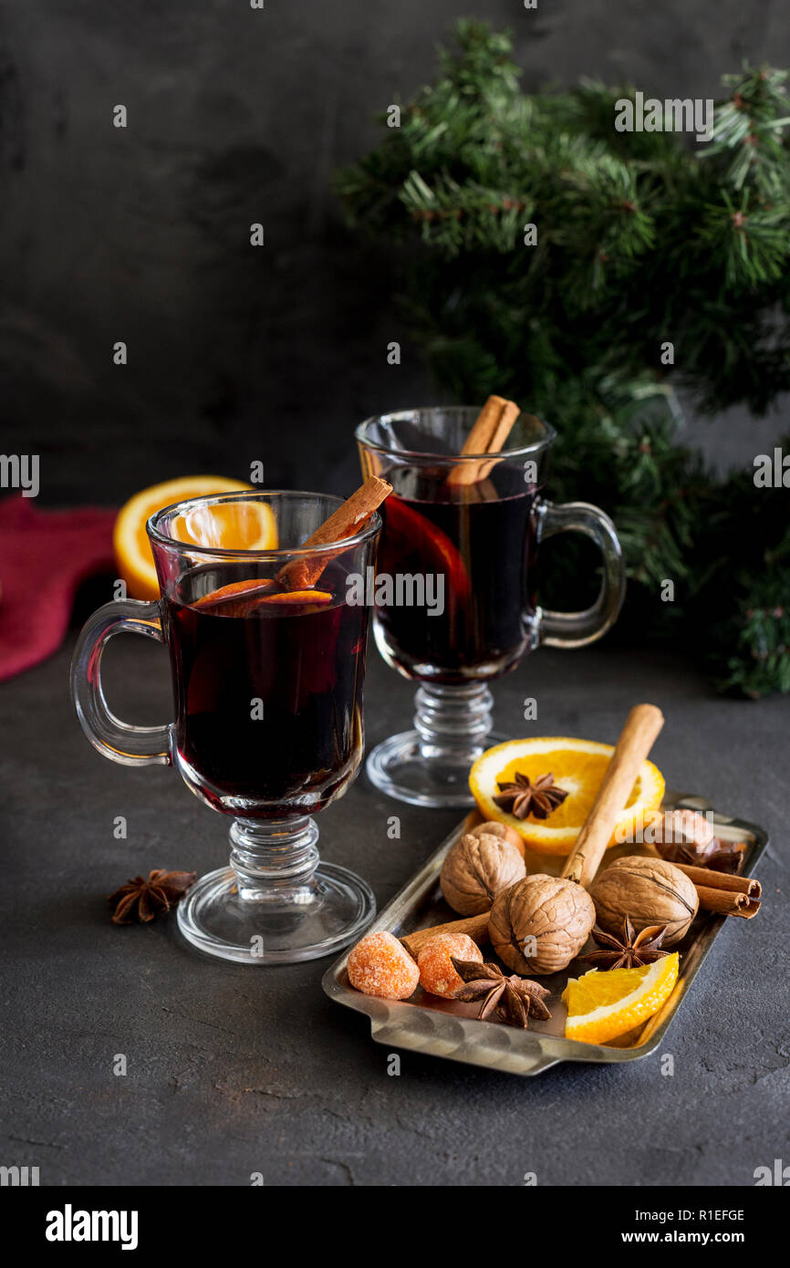 Winter Weihnachten Komposition. Rote Glühwein in Gläsern auf schwarzen Hintergrund. Tanne Kranz, Orange, Zimt, Nüssen, Kegel und Gewürze in der Nähe. Stockfoto
