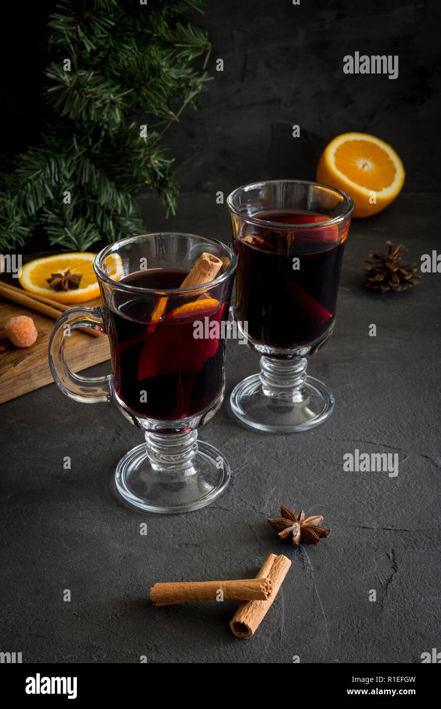Winter Weihnachten Komposition. Rote Glühwein in Gläsern auf schwarzen Hintergrund. Tanne Kranz, Holz mit Orange, Zimt, Nüssen, Kegel und Gewürze in der Nähe von Stockfoto
