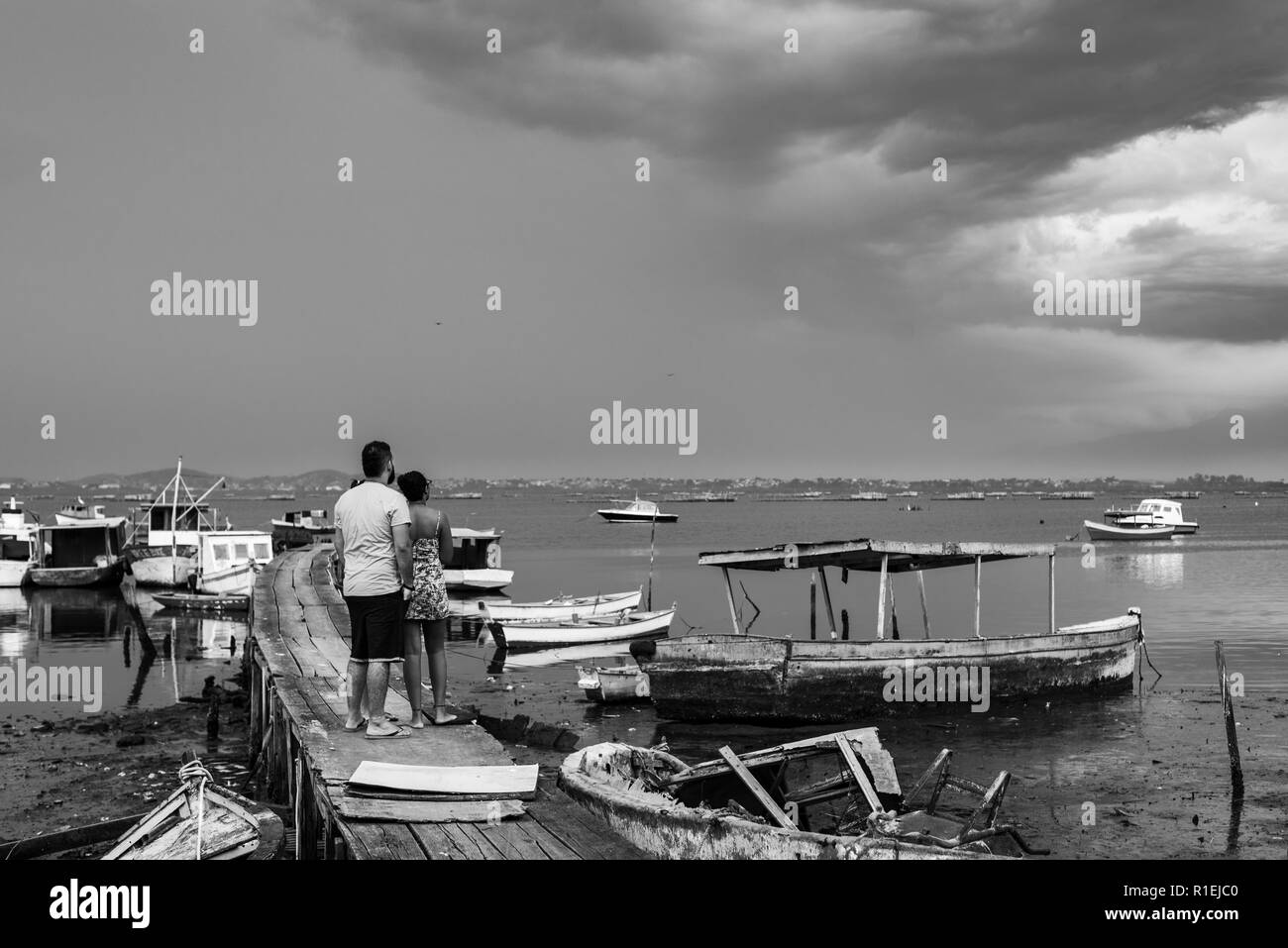 Ein junges Paar umarmen auf einem Pier zum Horizont der Guanabara-bucht in Rio de Janeiro, Brasilien suchen, mit Trödel Boote um. Stockfoto