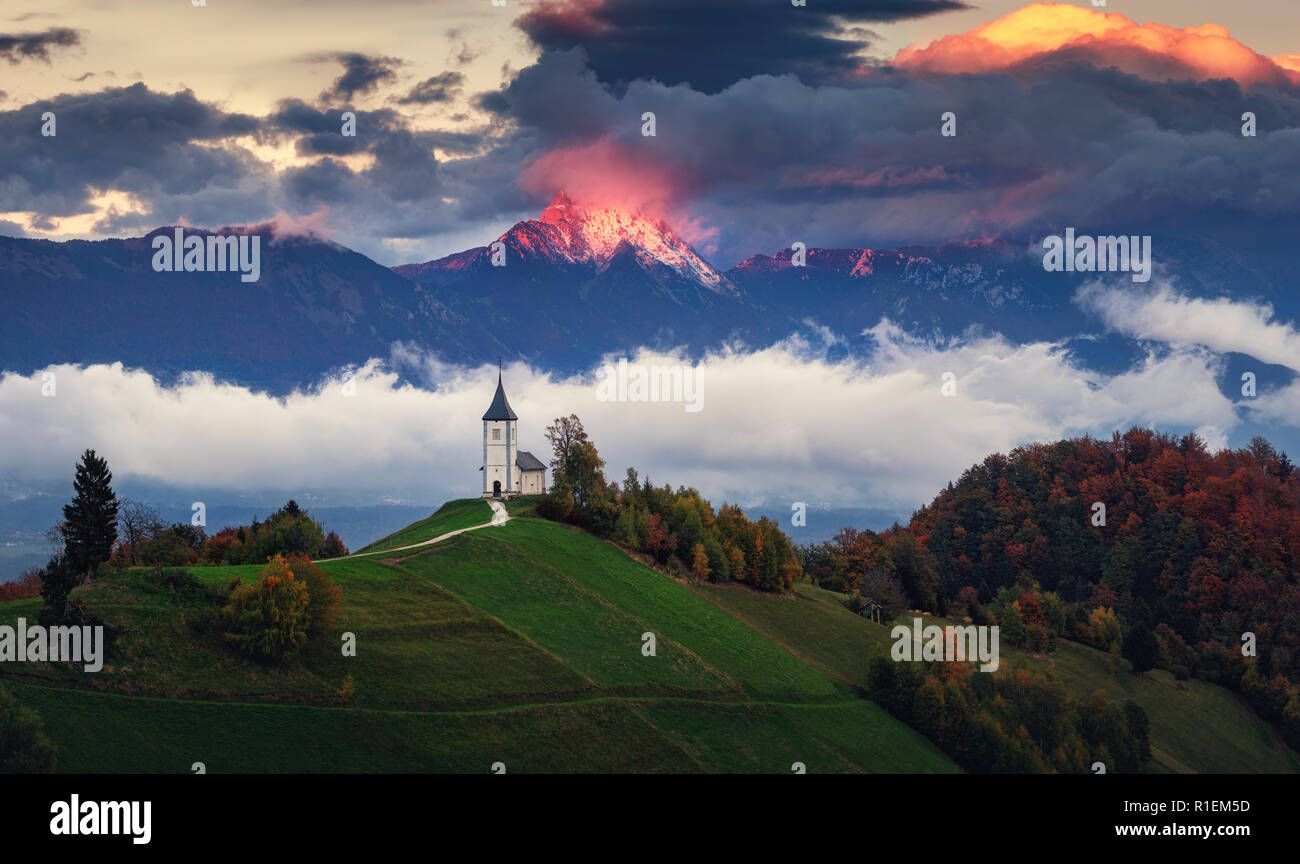 Jamnik, Slowenien - Panoramablick auf Regenbogen über der Kirche St. Primoz in Slowenien in der Nähe von jamnik mit schönen Wolken und die Julischen Alpen im Hintergrund Stockfoto