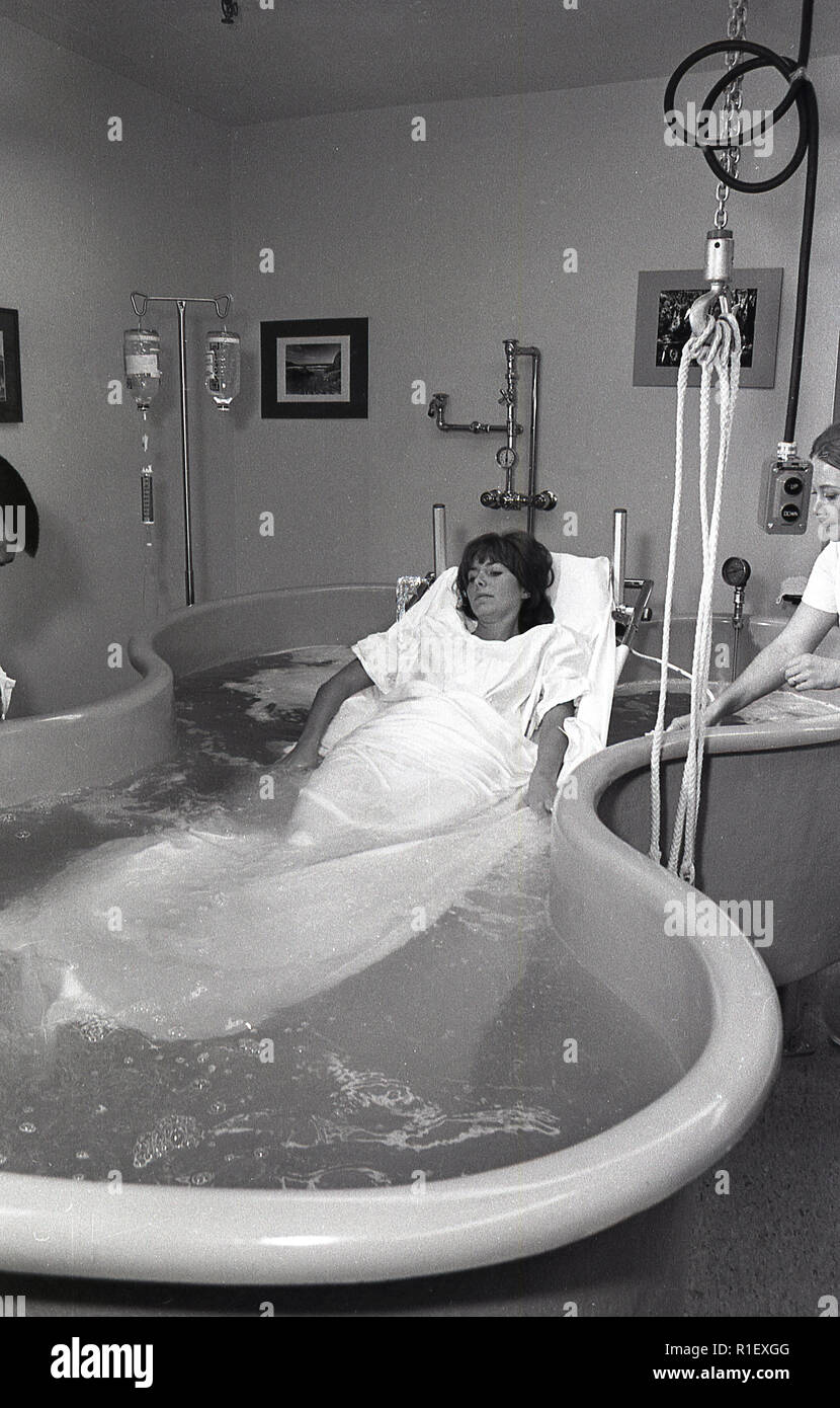 1970 s, historische, in einem Zimmer in einem LA Hospital, einem erwachsenen weiblichen Patienten auf einer Bahre aus Metall, das sich in einem großen Whirlpool Wanne mit Wasser, Hydrotherapie, unterstützt durch eine Krankenschwester, Los Angeles, USA. Stockfoto