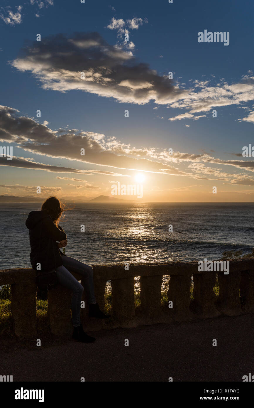 Frau sitzt an der Wand mit Blick auf den Atlantischen Ozean bei Sonnenuntergang. Stockfoto