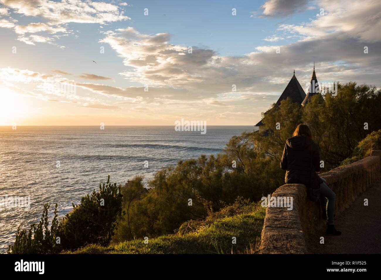 Frau sitzt an der Wand mit Blick auf den Atlantischen Ozean bei Sonnenuntergang. Stockfoto