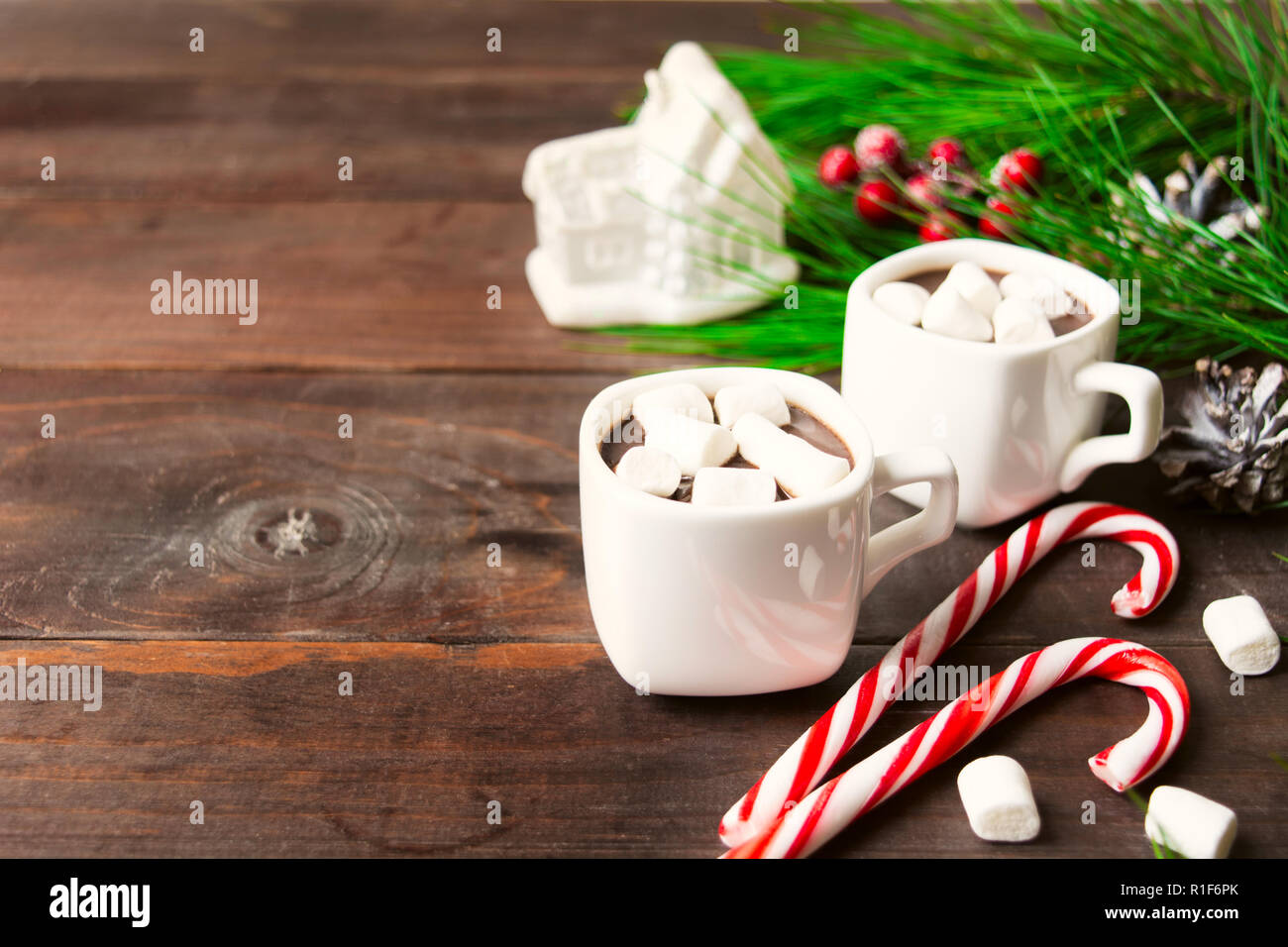 Zwei heiße Getränke mit Marshmallow in Cups mit Spielzeug Haus und zwei Zuckerstangen, Weihnachten Getränke auf Holz- Hintergrund mit Kopie Raum Stockfoto