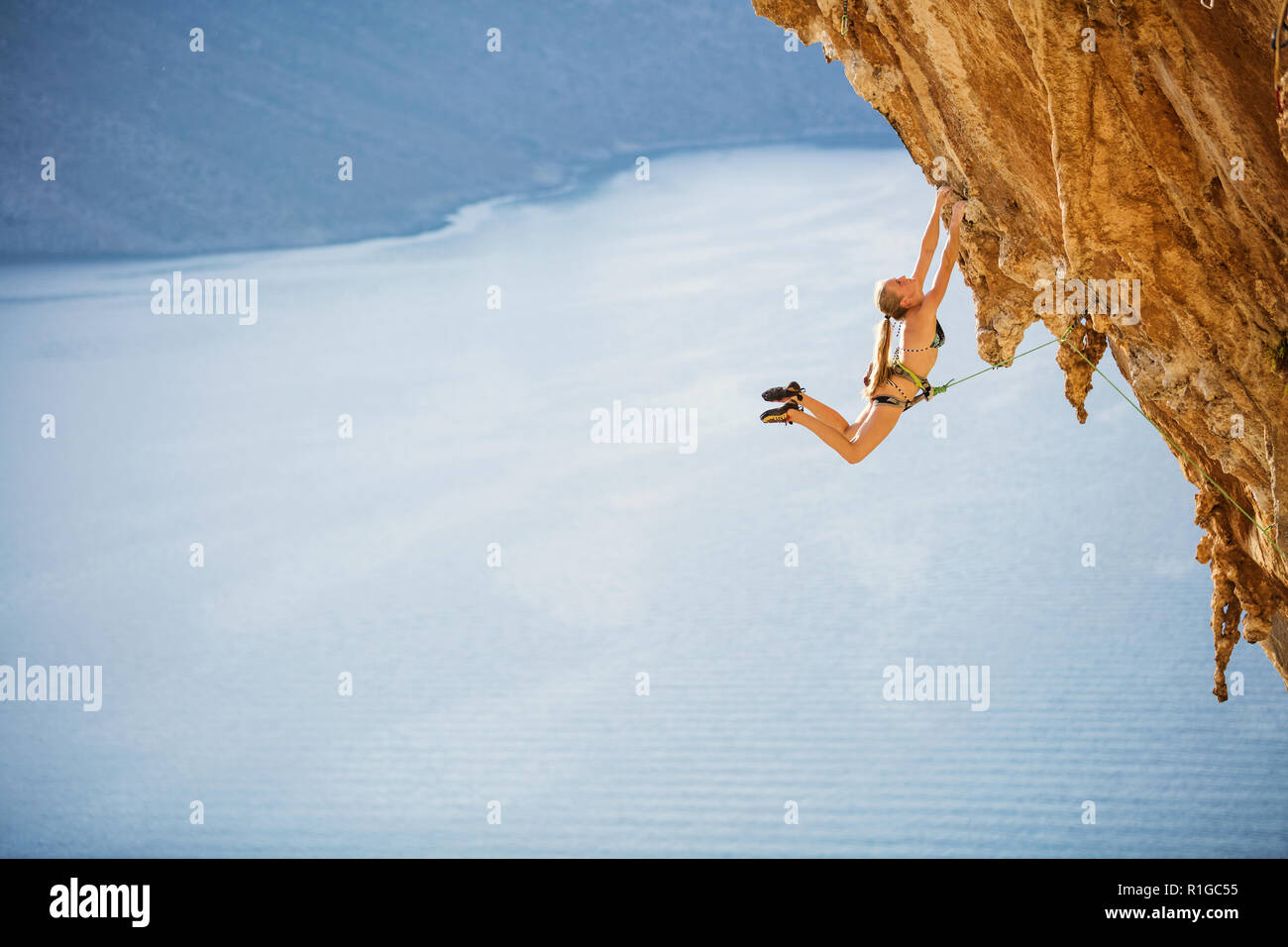 Female Rock climber Springen auf haltegriffe auf anspruchsvolle Strecke auf einer Klippe, mit Blick auf das Meer und die Küste Stockfoto