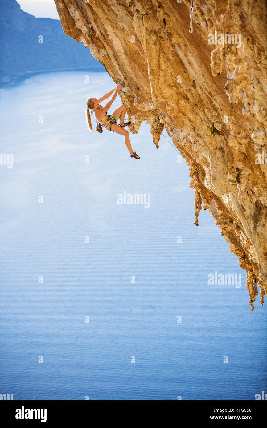 Junge weibliche Kletterer auf anspruchsvolle Strecke auf einer Klippe mit Blick auf das Meer und die Küste Stockfoto