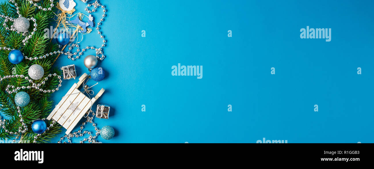 Weihnachten Grenze von Zweigniederlassungen, Fichte, silber Girlanden, blau und silber Weihnachten Kugeln und kleinen hölzernen weißen Schlitten. Flach. Festlicher Rahmen für Gree Stockfoto