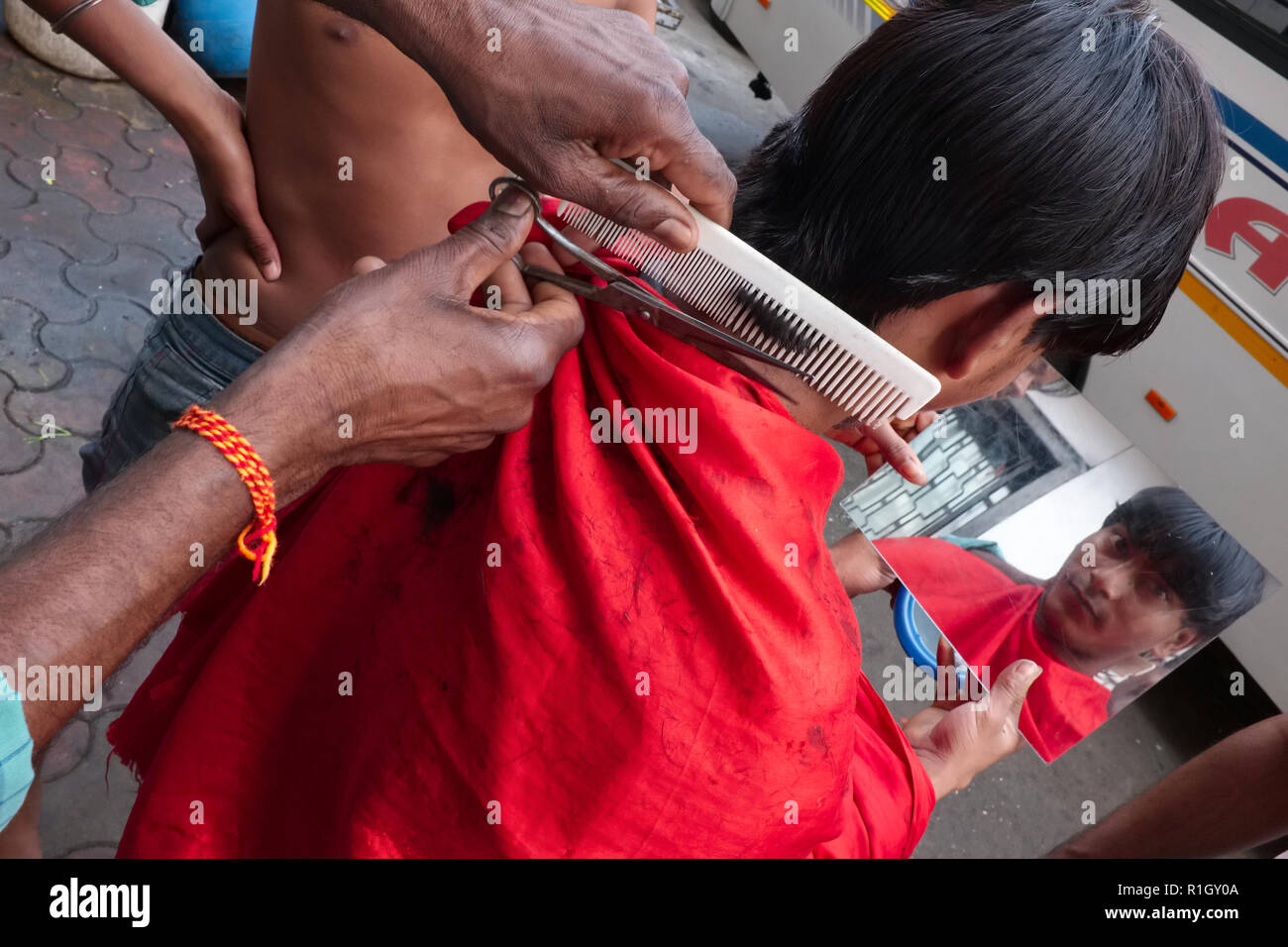 In einem Open-air-Friseur ist auf einem Bürgersteig in Mumbai, Indien, der Kunde überwacht die Arbeiten der Friseur in einem Spiegel Stockfoto