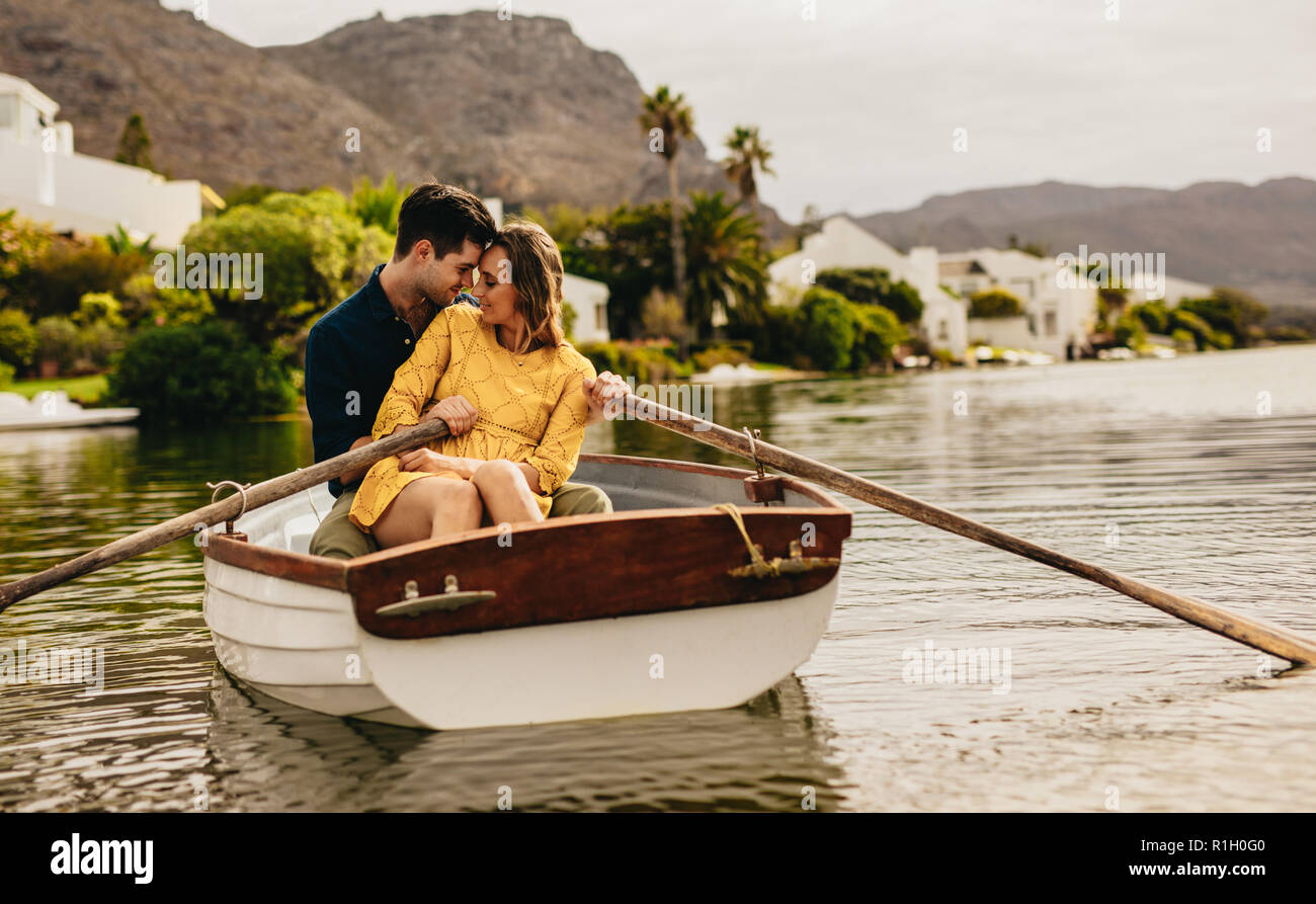 Romantisches Paar sitzen in einem Boot, ihre Köpfe zu berühren. Paar auf einem Boot Datum in einem See mit Hügeln und Häuser im Hintergrund. Stockfoto