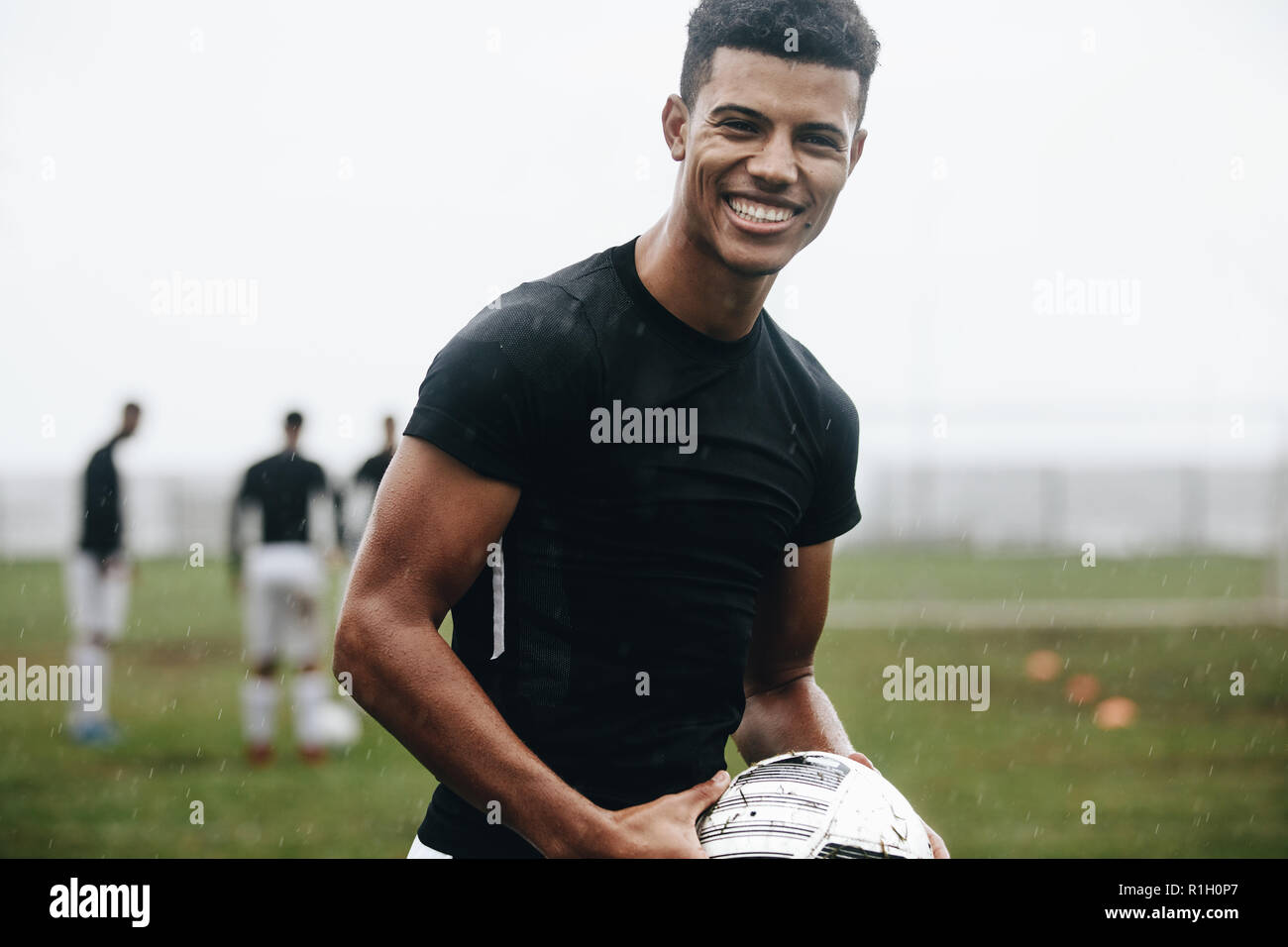 Porträt eines lächelnden footballer stehen auf Feld in Regen. Fröhliche Fußball-Spieler üben in den Morgen auf Feld mit Mannschaftskameraden spielen in der Ba Stockfoto