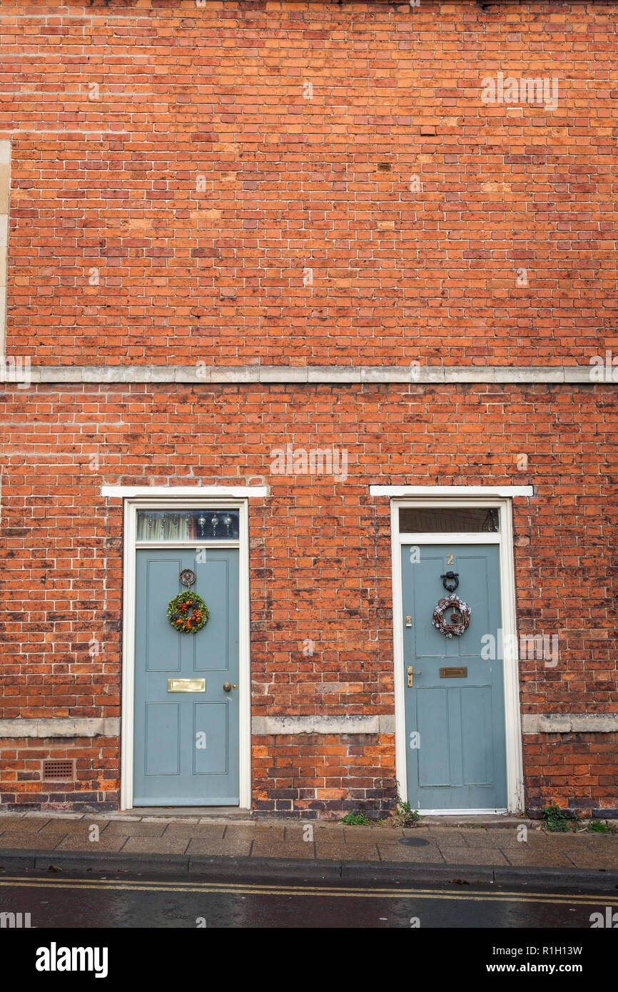 Zwei alte Türen in einem Ziegelstein Terrasse der Häuser haben beide Weihnachten Kränze befestigt. Stockfoto