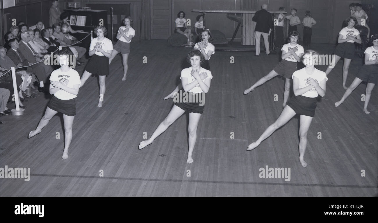 1940 s, historischen, einer Gruppe von High School für junge Frauen in nackten Füsse und das Tragen von PE-Kit, ein Fitnessstudio akrobatische Bildung Tanz in einer Sporthalle vor beobachten Eltern, USA. Stockfoto