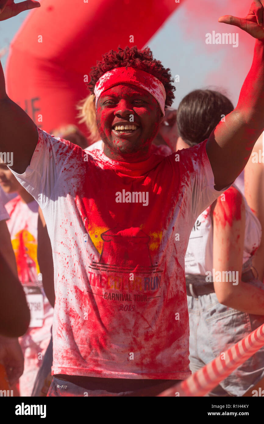 Portrait von schwarzen afrikanischen Mann mit Bügel Anheben der Arme im Triumph Farbe spritzt in roter Farbe beim Fun Run Sport Event in Kapstadt im Sommer Stockfoto