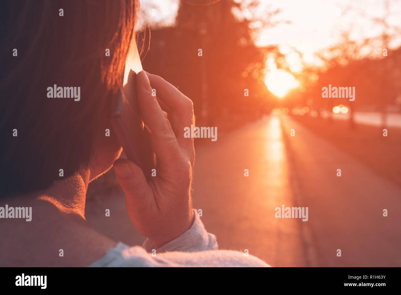 Frau Gespräch am Handy auf der Straße im Sonnenuntergang, Ansicht der Rückseite der Erwachsenen kaukasischen weibliche Person holding Smartphone Stockfoto