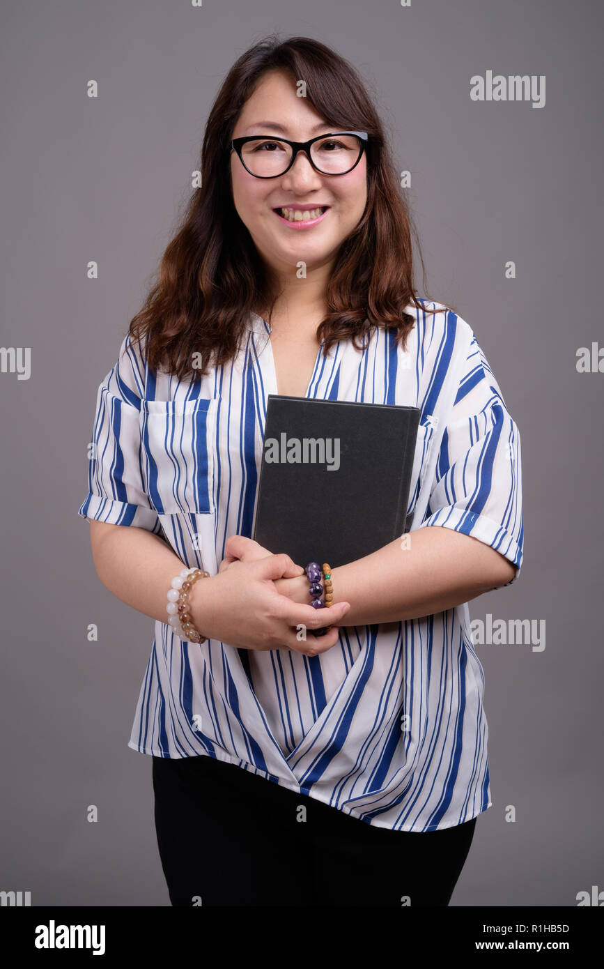 Asiatische Geschäftsfrau holding Buch gegen grauer Hintergrund Stockfoto